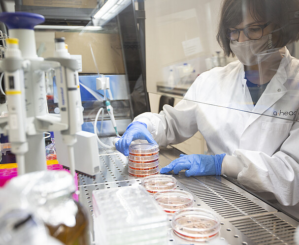 Woman wearing a mask in a laboratory surrounded by scientific equipment looking at petri dishes