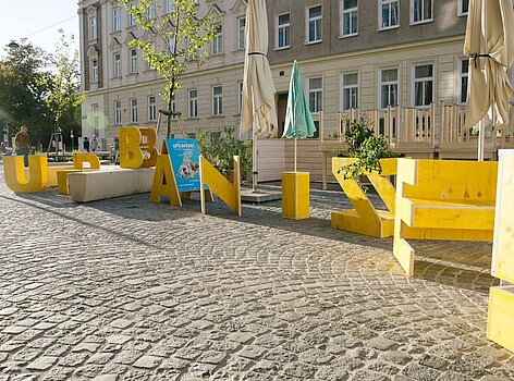 Vor einem Gebäude stehen große, gelbe Holzbuchstaben, die das Wort Urbanize bilden. 