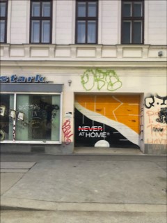 Never At Home: Garageneinfahrt in einer Straße auf der das Never At Home Logo zu sehen ist.
